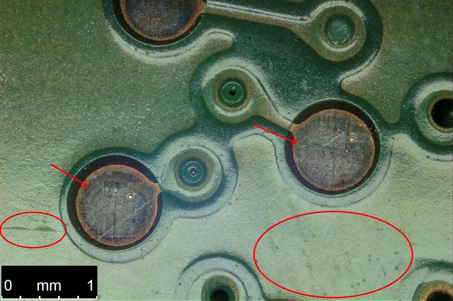 [Translate to chinese:] Image of the same portion of the PCB shown in Fig. 4a. The image was recorded with the DVM6 using integrated coaxial oblique illumination and 1/4 wave plate with relief contrast. Notice the scratches and defects on the pads (arrows) and imperfections and variations on the substrate (encircled areas) become more visible compared to the ring light illumination (Fig. 4a).