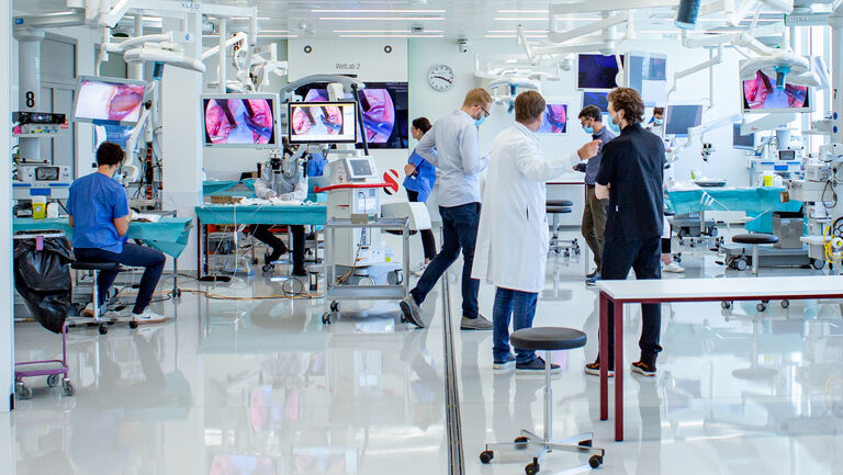 图像来自瑞士日内瓦瑞士国际外科手术创新和培训基金会 (SFITS)。在实操练习课上，老师通过 3D 4K 大屏幕为整个实验室演示手术技巧，指导参与课程的学生。

